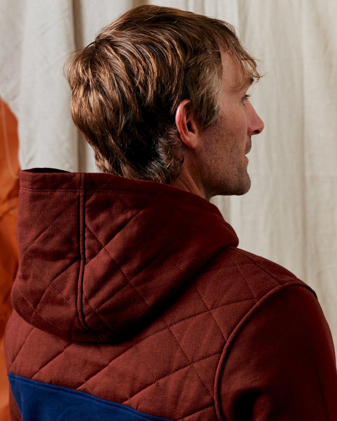 Side view of a person with short brown hair wearing the Saltrock Aiken - Men's 1/4 Neck Recycled Hoodie in red, standing against a light-colored background.