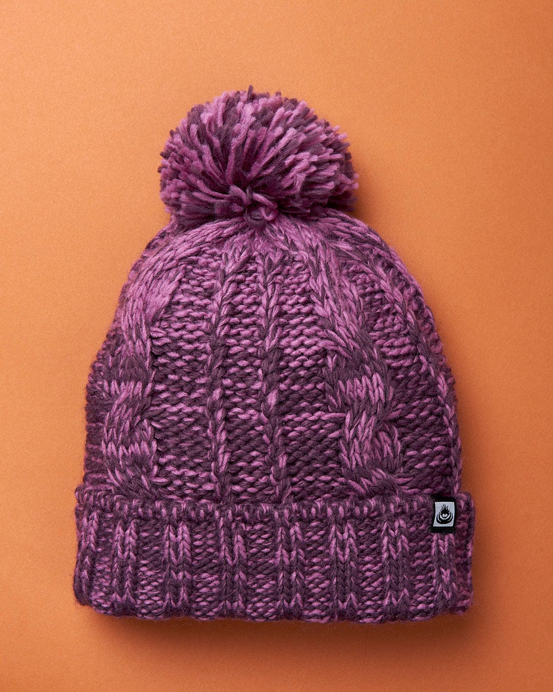 A Twist - Cabled Beanie - Dark Pink from Saltrock on an orange background.