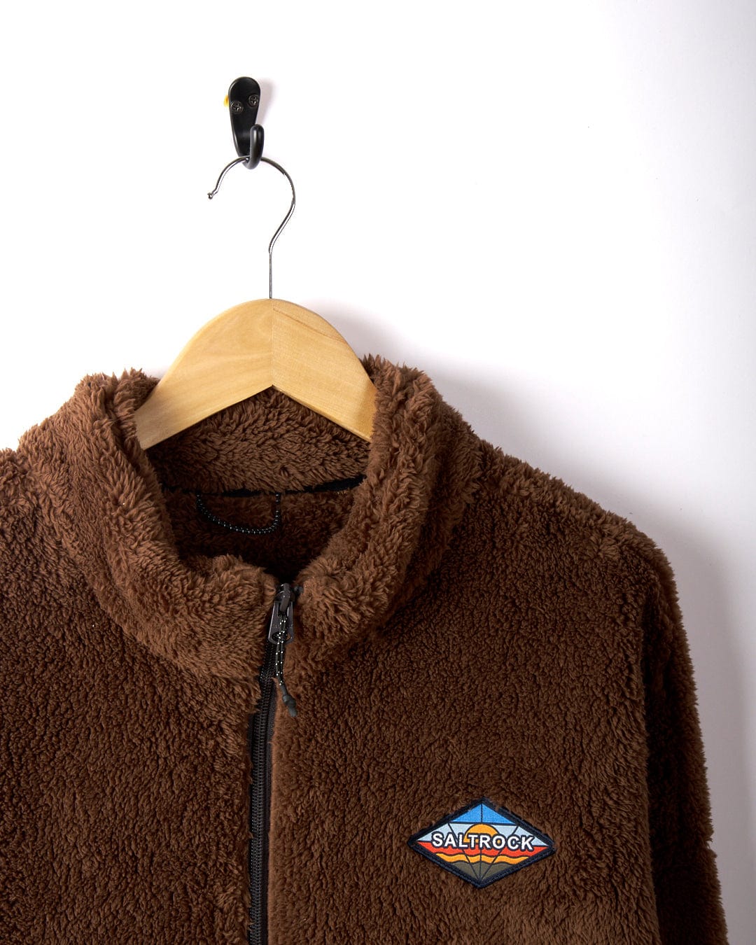 Brown Saltrock Arches men's recycled oversized fleece jacket on a wooden hanger, showcasing the front logo, made from recycled materials against a plain white background.