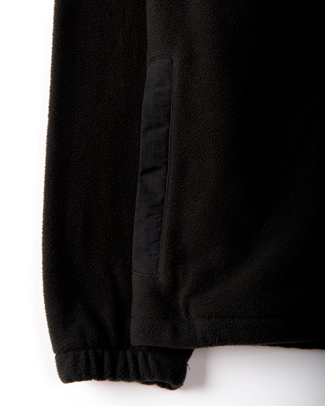 Close-up of the sleeve from the Ava women's fleece jacket by Saltrock, showcasing black microfibre material crafted from recycled yarns, with an elastic cuff and a vertical pocket against a white background.