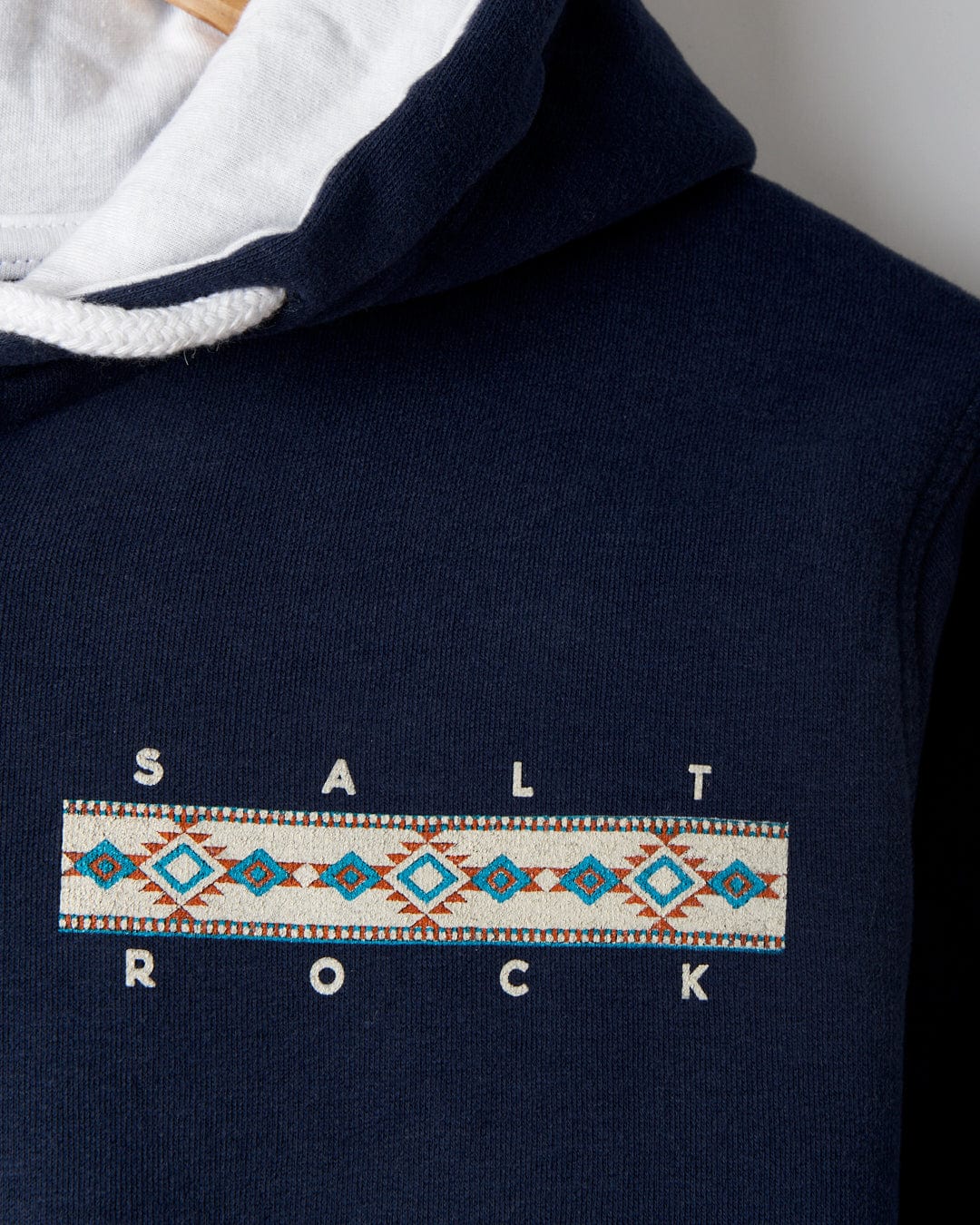 The Aztec Mountain Women's Zip Hoodie by Saltrock showcases iconic branding with "SALT ROCK" text and a geometric pattern in blue, teal, and orange. It features a drawstring hood, capturing the essence of a cosmic mountain scene effortlessly.