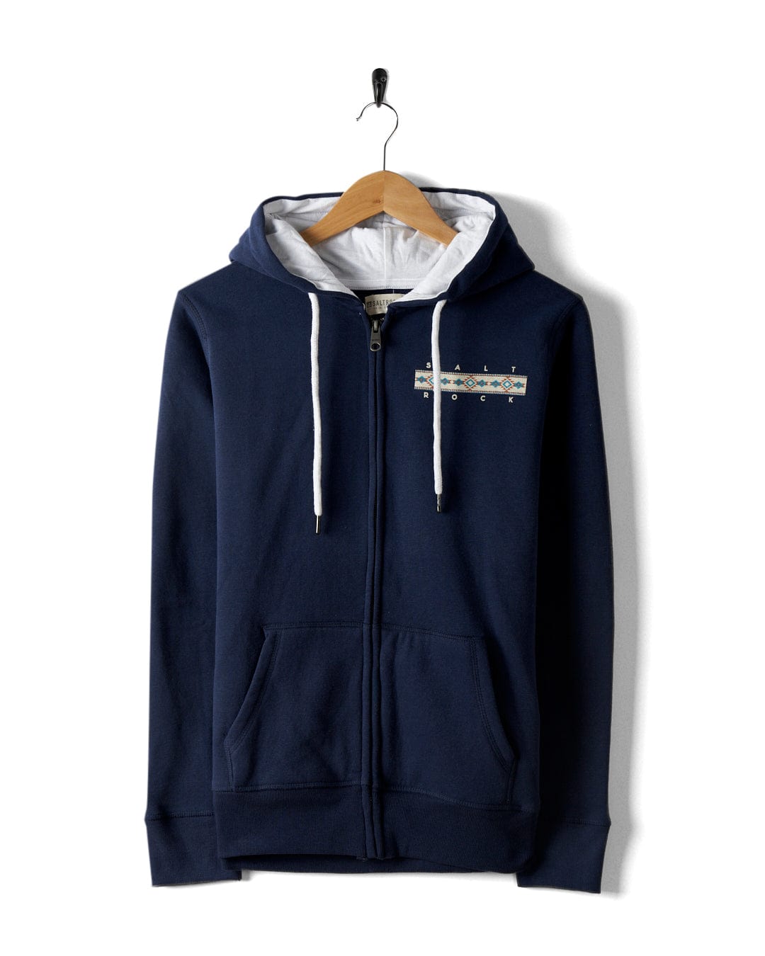 The Aztec Mountain Women's Zip Hoodie in blue by Saltrock, featuring a small geometric pattern on the chest, has white drawstrings and front pockets. It hangs on a wooden hanger against a white background.