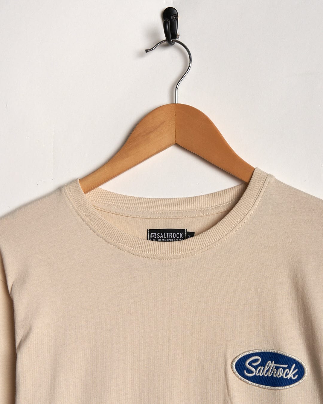 Cream long-sleeve t-shirt on a wooden hanger against a white background, featuring the 