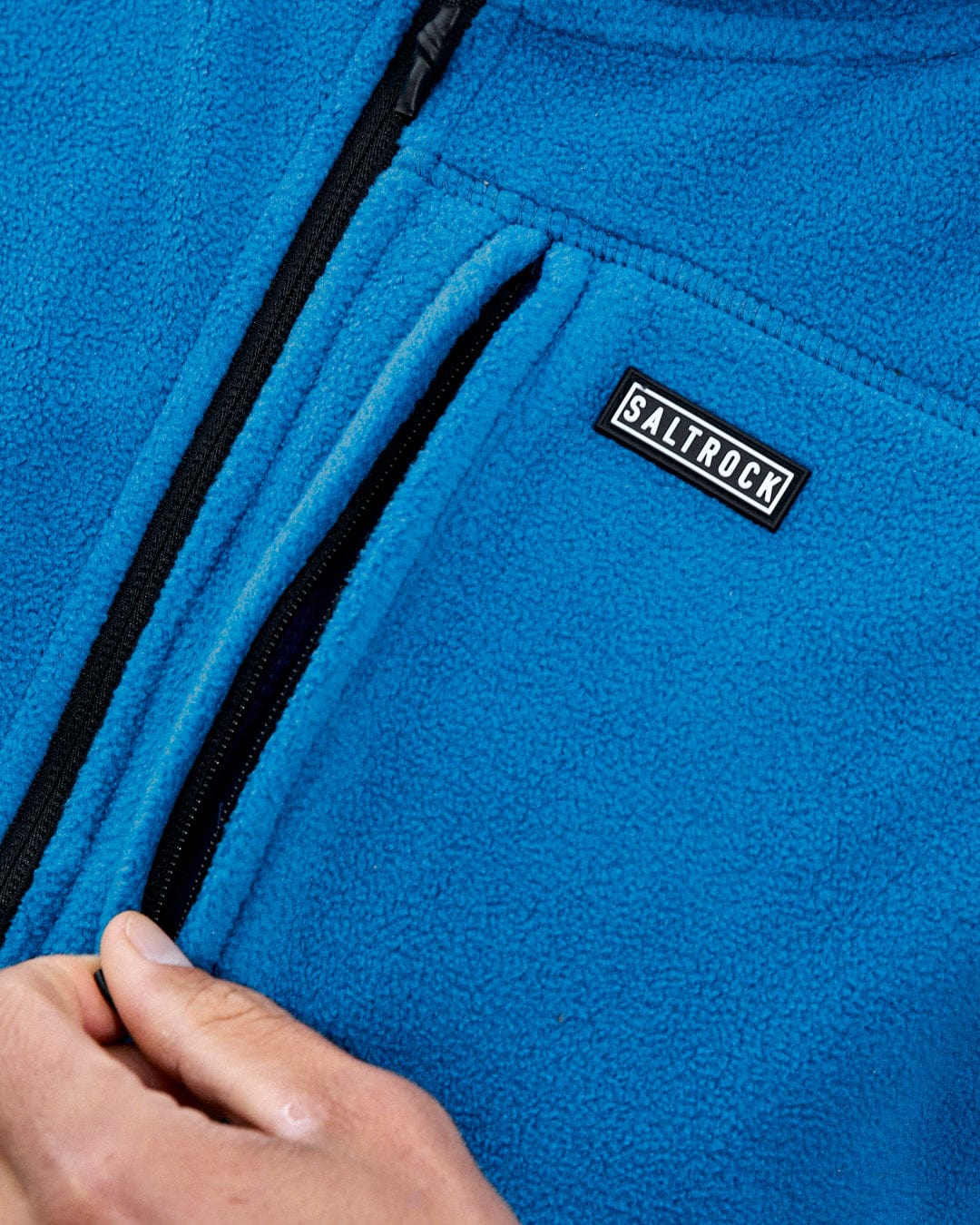 A person is unzipping the Saltrock Bradford fleece jacket in blue, made from thick recycled polyester and showcasing a logo on the chest.