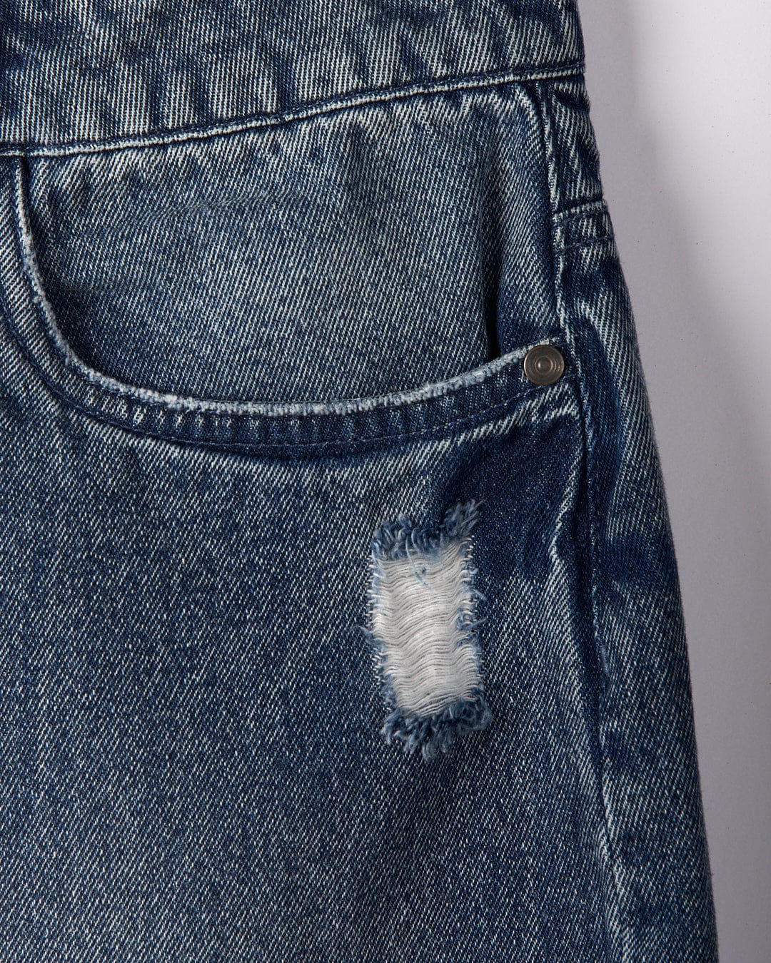 Close-up of a portion of the Brittany women's high-waisted denim shorts by Saltrock in blue, featuring a small frayed tear above the right pocket that showcases their distressed denim charm.