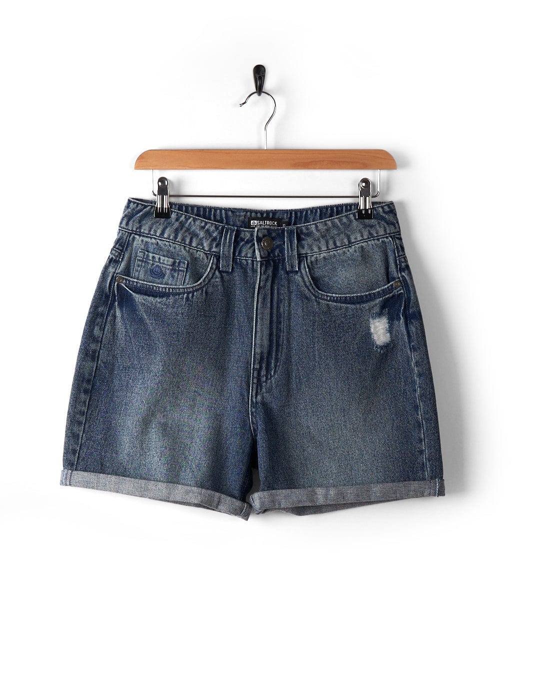 Brittany - Women's High Waisted Denim Shorts by Saltrock, featuring rolled cuffs, five pockets, and a distressed detail on the right thigh in a light vintage stone wash, hanging on a wooden hanger against a white background.