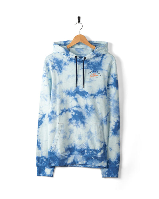 A blue and white tie-dye hoodie made from 100% cotton with front pockets and a drawstring hood hangs on a wooden hanger against a white background, showcasing the Saltrock Coastline - Mens Tie Dye Pop Hoodie - Blue.