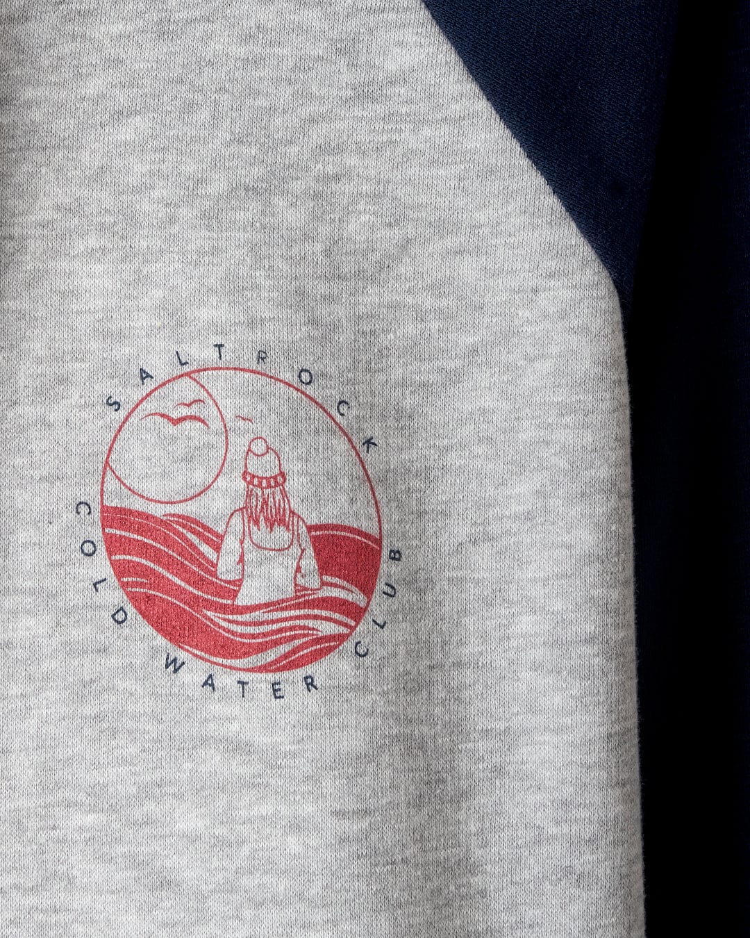 The Saltrock Coldwater Club Women's Raglan Pop Hoodie in grey features contrasting sleeves and a red circular logo showcasing a person in a beanie facing the waves and moon, along with "Saltrock Cold Water Club" graphics.