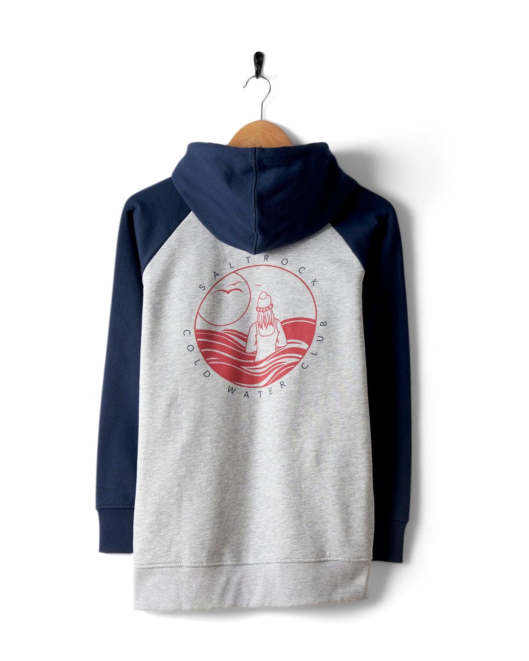 A Saltrock hoodie, named Coldwater Club - Womens Raglan Pop Hoodie - Grey, features navy raglan sleeves and a gray body. It hangs on a hook, sporting bold Cold Water Club graphics on the back with a red image of someone in water and the text "Saltrock Cold Water Club.