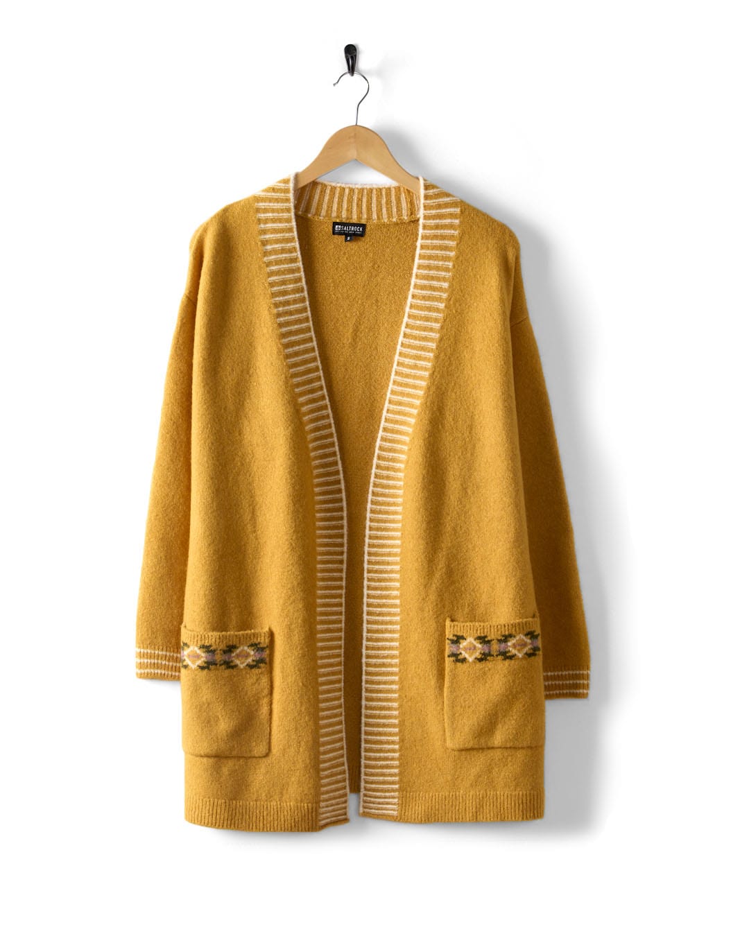 The Saltrock Coraline Women's Longline Knitted Cardigan, in yellow, hangs elegantly on a wooden hanger. It features white-edged open-front styling with two front pockets adorned with an Aztec pattern for added detail.