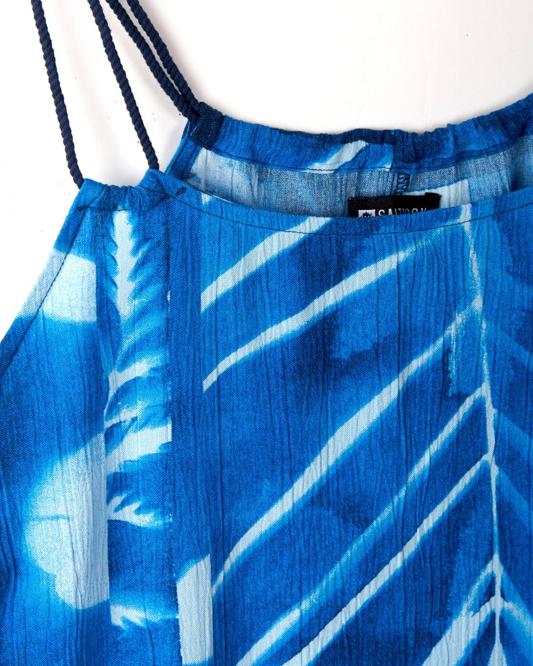 Close-up of a Cyanotype - Womens Cami - Blue by Saltrock with white abstract floral print and thin shoulder straps made from lightweight material. A black clothing label is partially visible inside the neckline.
