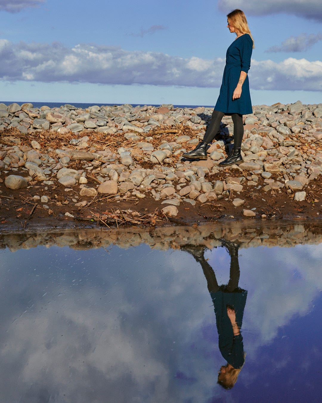 A fashion-conscious woman standing next to a puddle of water wearing a Saltrock Della Womens Wrap Top Dress in Dark Blue.