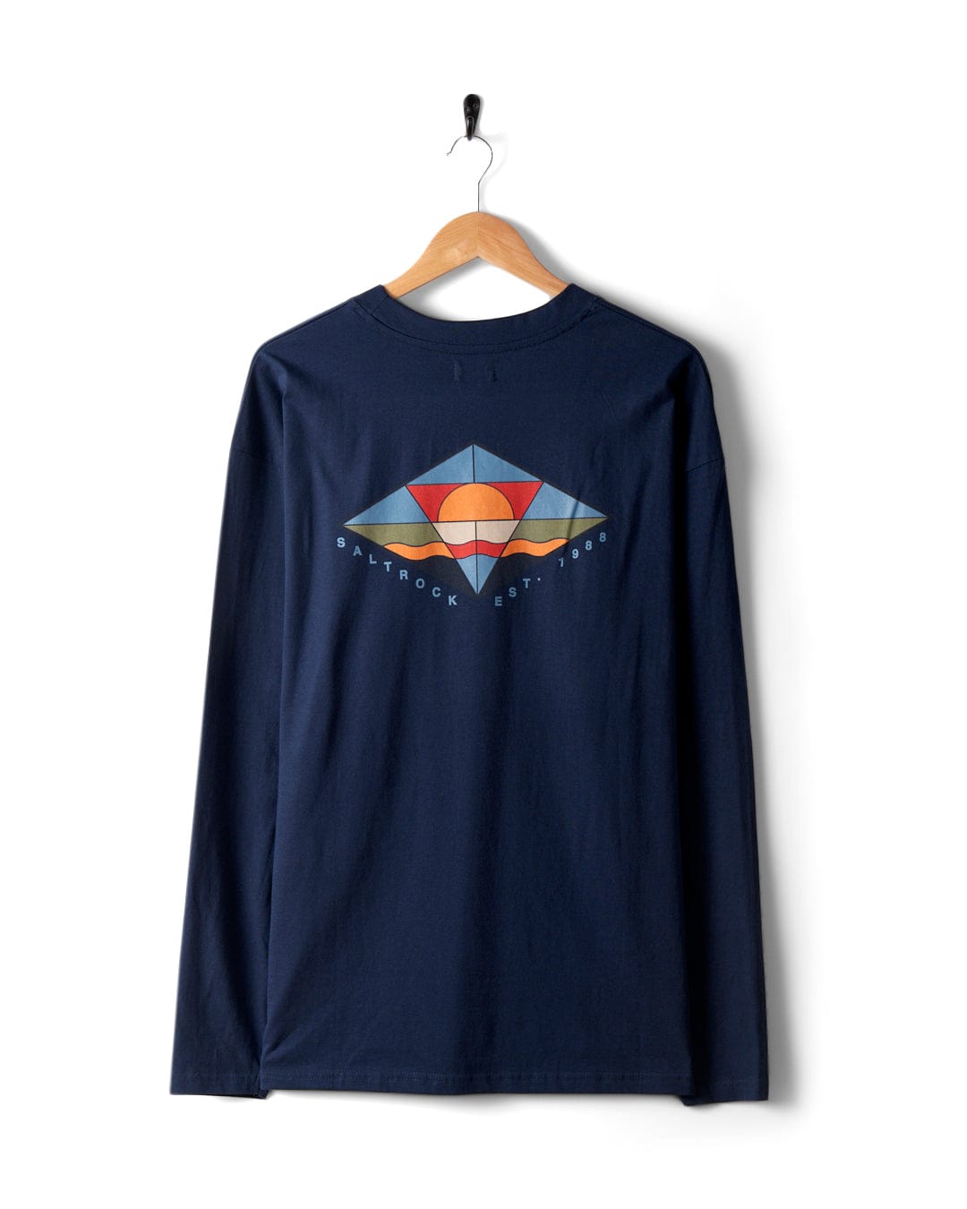 The Saltrock Dimensions Colour 2 men's long-sleeve T-shirt in blue is crafted from 100% cotton and adorned with vibrant sunrise prism graphics of a sunset and mountains on the back. Displayed on a wooden hanger, the shirt features text that reads "Saltrock Est. 1988.