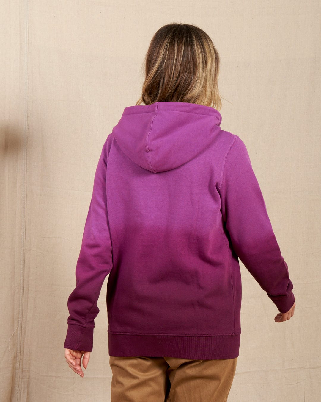 A person wearing the Saltrock Dip Dye Women's Zip Hoodie in purple, paired with tan pants, stands with their back to the camera against a plain background. The hoodie boasts a subtle dip dye print for added style.