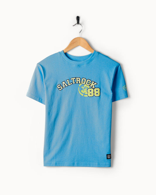 A light blue Drop Out - Kids T-Shirt - Blue with the word "Saltrock" and the number "88" in bold letters on the front. Crafted from 100% cotton, this shirt is machine washable for easy care. It's displayed on a wooden hanger against a white background, showcasing its classic Saltrock branding prominently.