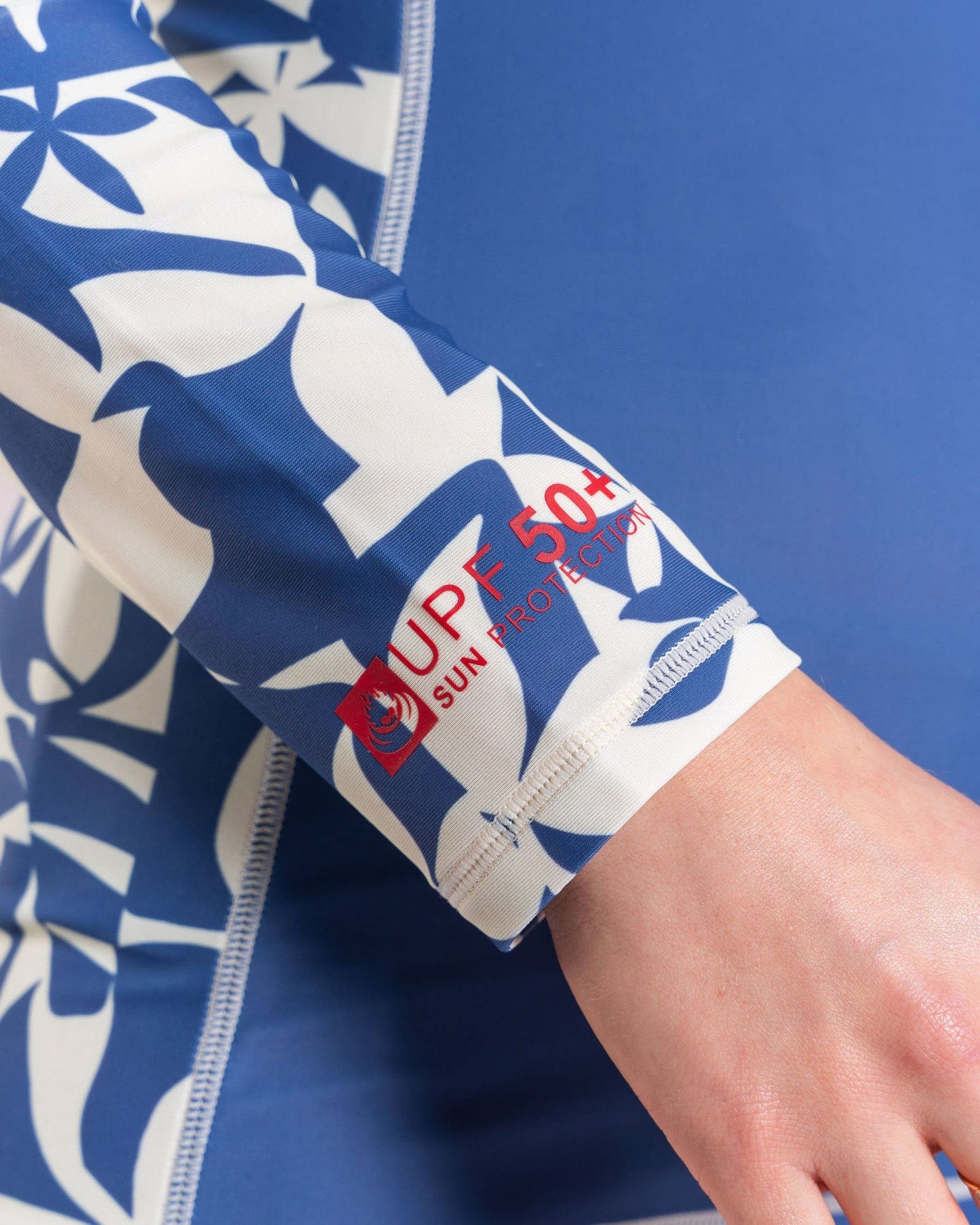 A close-up of Saltrock's Balance Women's UPF 50+ Rashvest in blue highlights its blue and white floral print, showcasing recycled polyester fabric on the sleeve label.