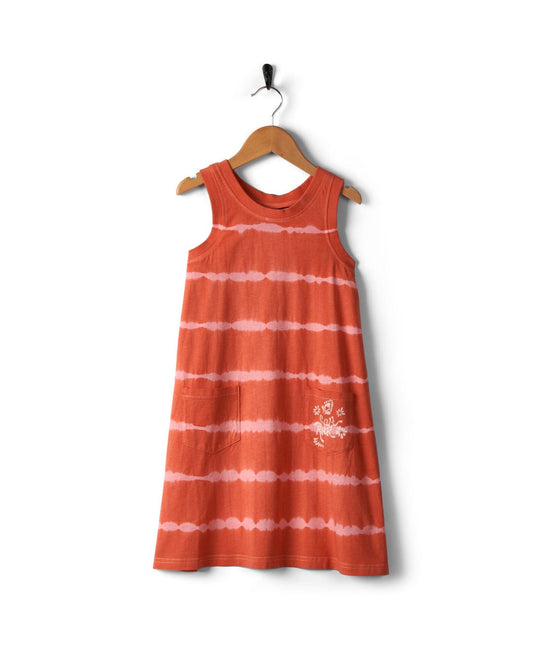 A Saltrock Eliana - Kids Tie Dye Vest Dress - Peach, hanging on a wooden hanger with a hook.
