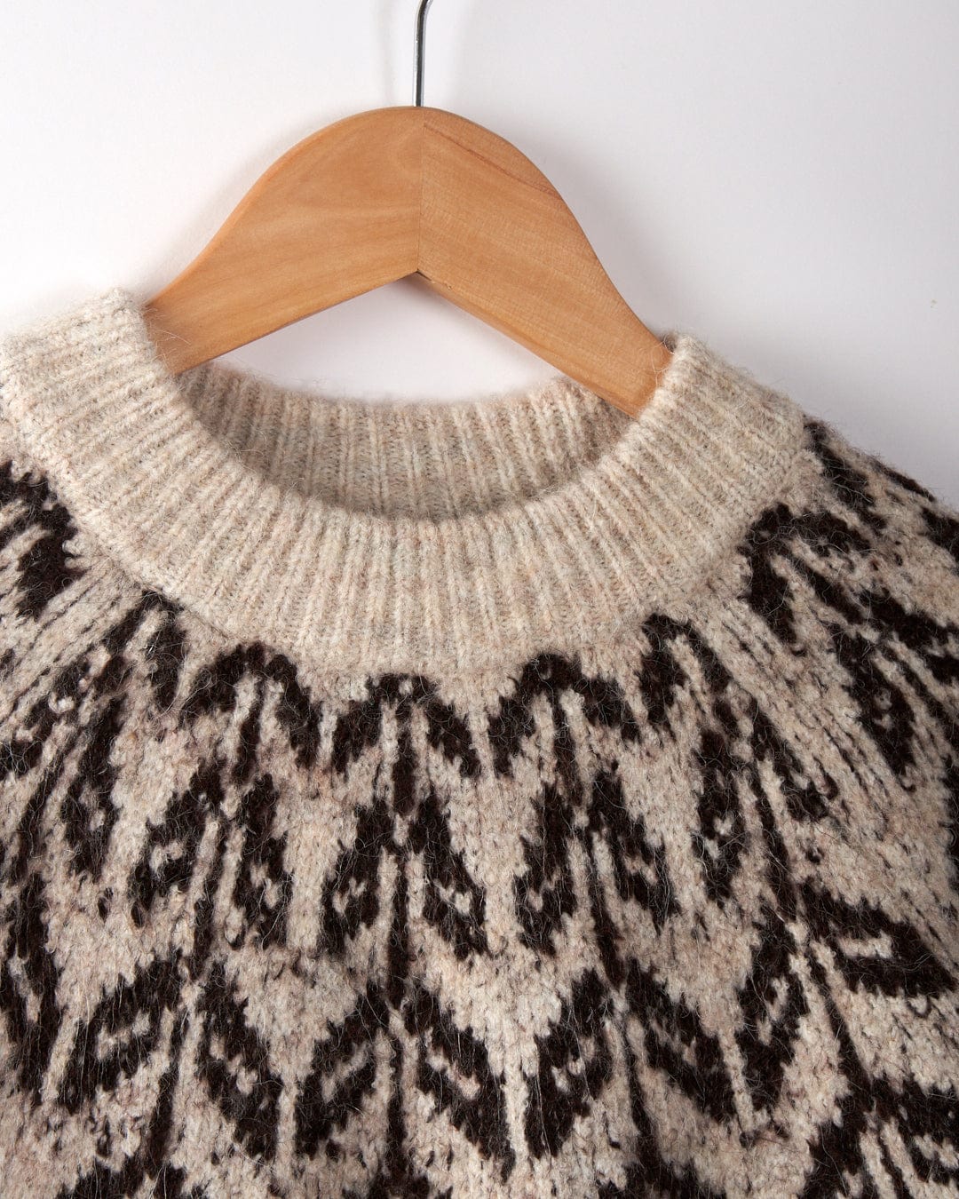 Saltrock's Fairisle Women's Knitted Jumper, featuring a geometric pattern in beige and brown, is displayed on a wooden hanger against a white background. This stylish crewneck combines coziness with the convenience of being machine washable.