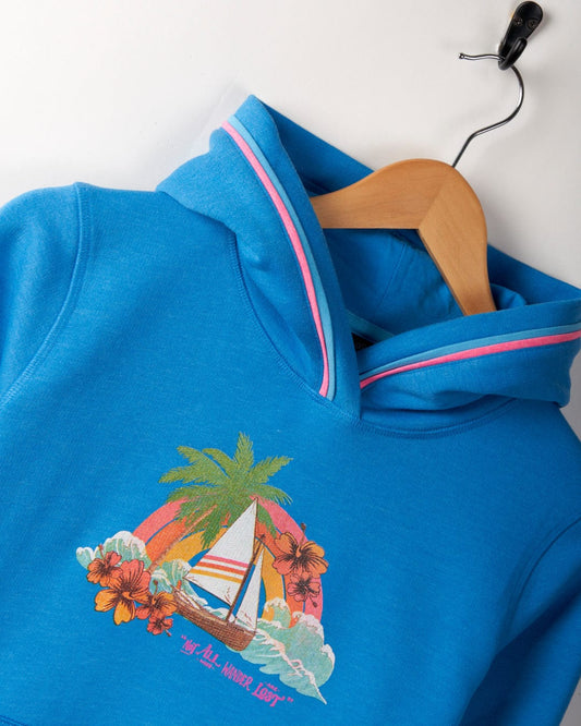 A Floral Lost Ships - Kids Recycled Pop Hoodie - Blue with Saltrock graphics, featuring a sailboat, palm tree, and flower design, hanging on a wooden hanger. It includes a convenient Kangaroo pocket for added functionality.