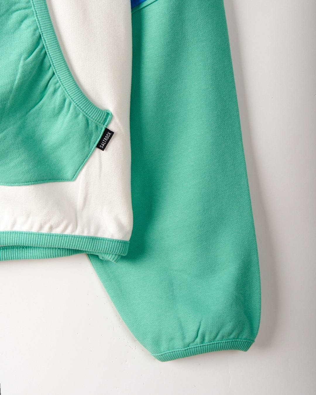 Close-up of a garment showcasing a section of a green and white hoodie with Saltrock Geo Beach - Womens Pop Hoodie - White graphics, featuring a pocket, ribbed cuff, and a small tag that reads "Sinner.