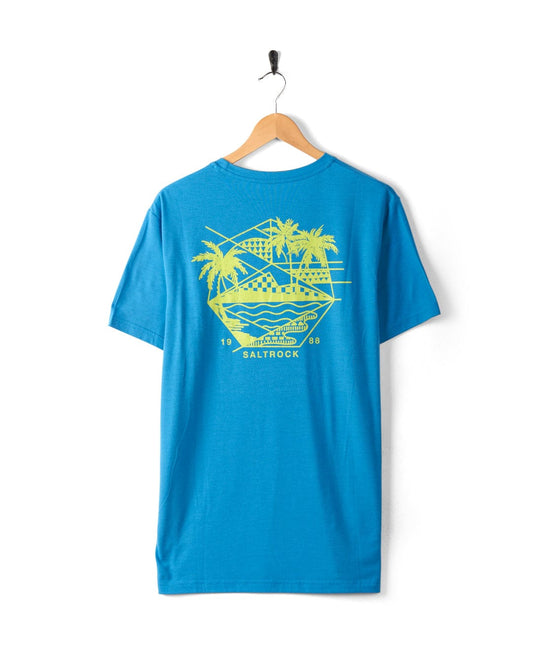 A Geo Palms Solid - Mens Recycled T-Shirt - Blue on a wooden hanger. The back features a yellow graphic of a scenic beach with palm trees and a sunset, along with the text "Saltrock" and "1988". Made from recycled material, this shirt has a cotton soft feel that is both comfortable and eco-friendly.