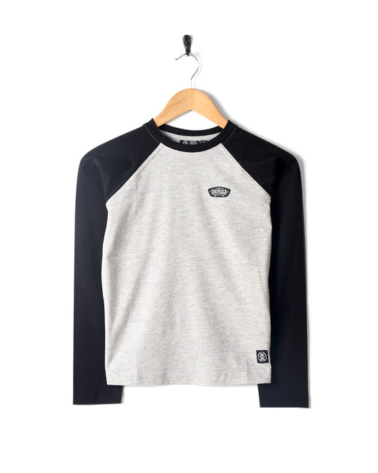 A grey and black long-sleeve raglan shirt with contrast sleeves on a wooden hanger, featuring a small patch design on the left chest and a Saltrock logo label near the hem. Machine washable for easy care.

Product Name: Hardskate Warp - Kids Longsleeve Raglan T-Shirt - Grey/Black

Brand Name: Saltrock
