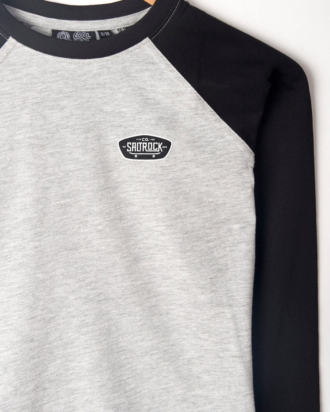 Close-up of a grey and black ***Hardskate Warp - Kids Longsleeve Raglan T-Shirt - Grey/Black*** with raglan contrast sleeves, featuring a small "Saltrock" logo on the left chest area. This stylish piece is machine washable for easy care.