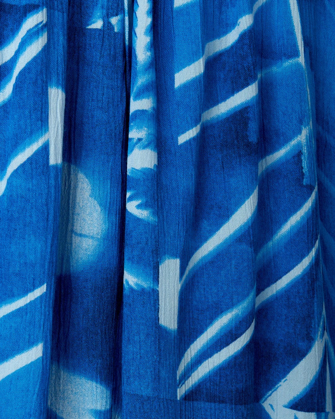 Close-up of a blue fabric with a textured surface and an abstract floral print, featuring white streaks and shapes from the Hesta - Womens Playsuit - Blue by Saltrock.