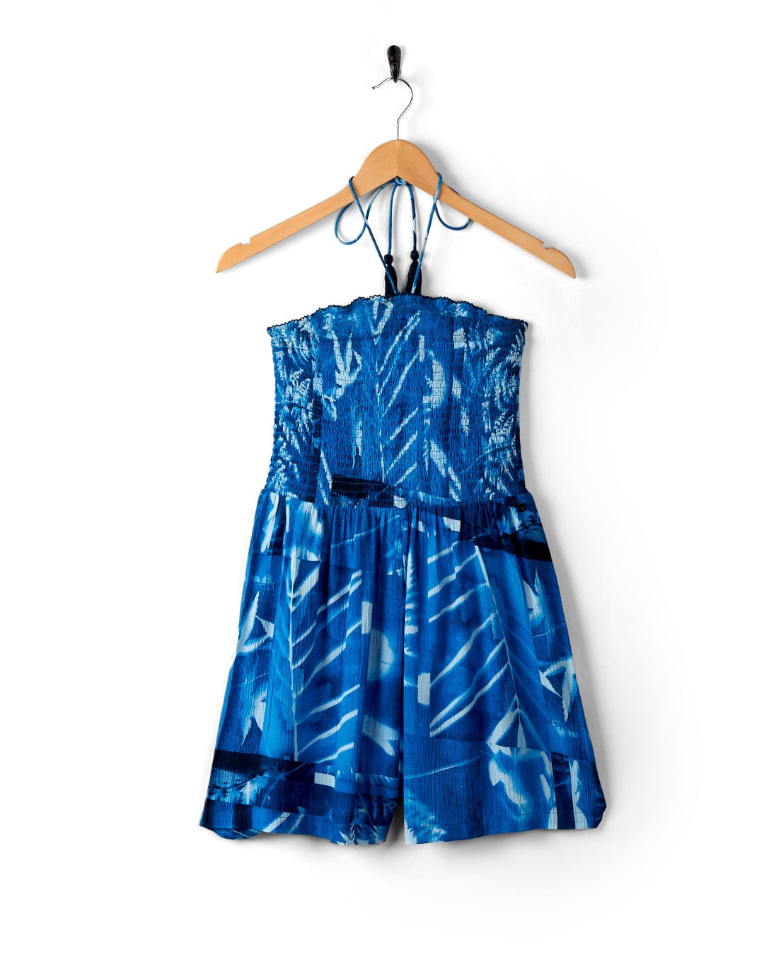 A Saltrock Hesta - Womens Playsuit - Blue with a tie-dye pattern and an abstract floral print, hanging on a wooden hanger against a white background.