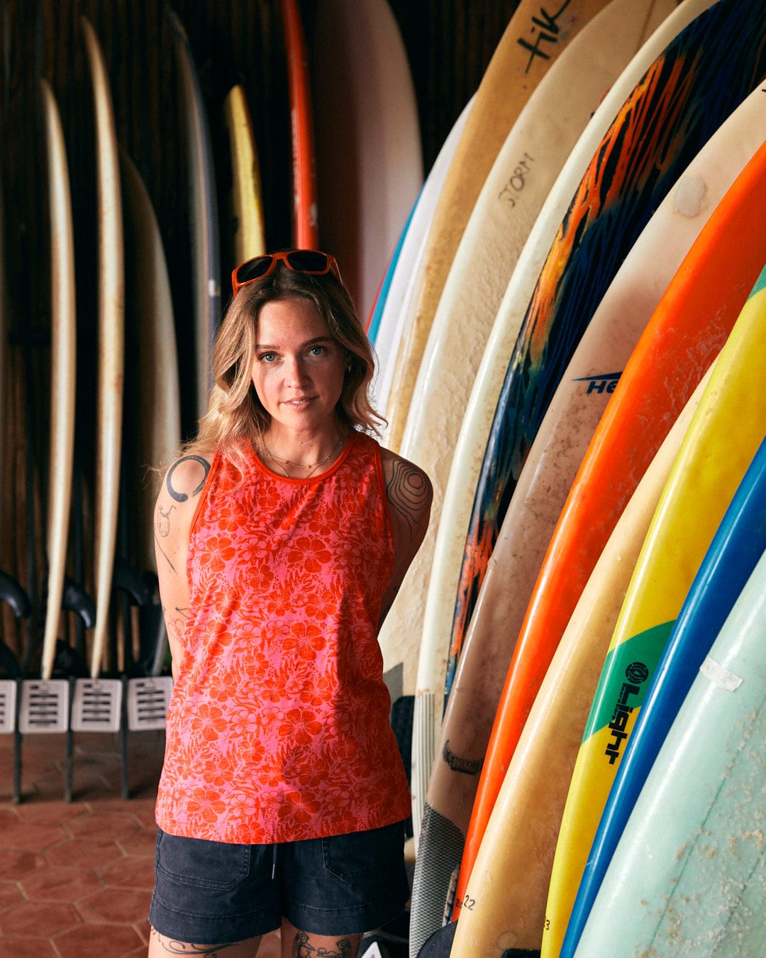 A person wearing a Saltrock Hibiscus - Womens Vest - Red and black shorts stands in front of an array of surfboards.