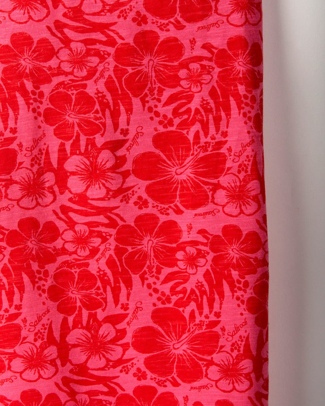 A close-up of bright pink, soft peached fabric adorned with a red floral pattern, featuring various flowers and leaves, including a delicate hibiscus print on the Hibiscus - Womens Vest - Red by Saltrock.