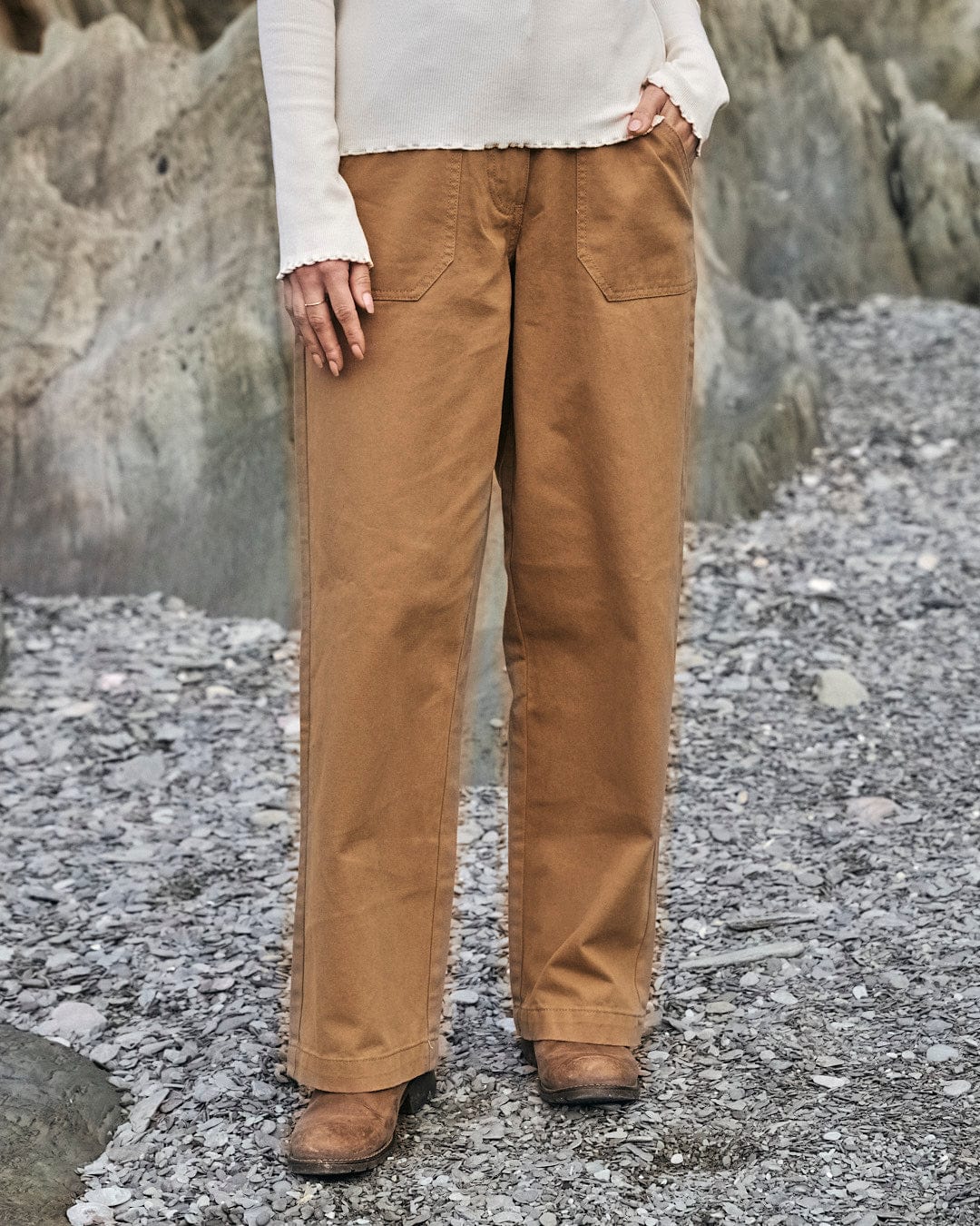 A woman is standing on rocks wearing Saltrock's Hilda Twill - Womens Trouser - Light Brown, offering comfort in 100% cotton.