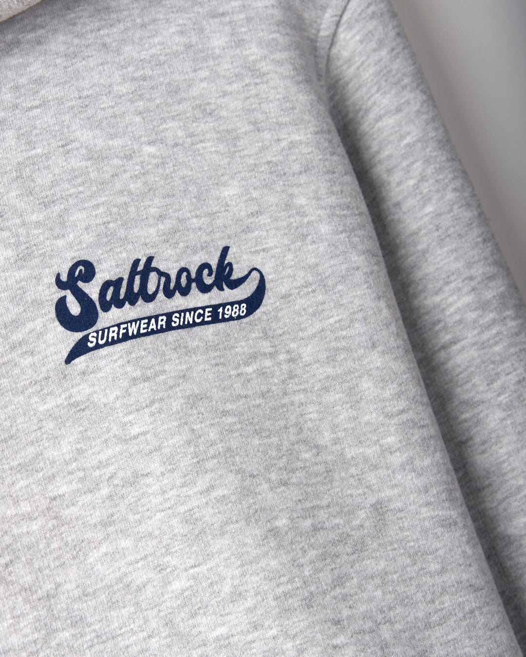 Home Run - Mens Zip Hoodie - Grey featuring the "Saltrock Surfwear Since 1988" logo in blue on the left chest area, complete with a hood with drawstrings. This stylish piece also boasts classic Saltrock branding and is conveniently machine washable for easy care.