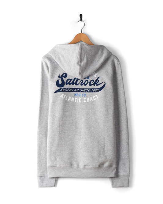 A grey hoodie hanging on a wooden hanger, featuring blue text and logo design on the back that reads "Saltrock Surfwear Since 1988" and "Atlantic Coast." Complete with Saltrock branding, it also boasts a hood with drawstrings and is machine washable for easy care. This is the Home Run - Mens Zip Hoodie - Grey by Saltrock.