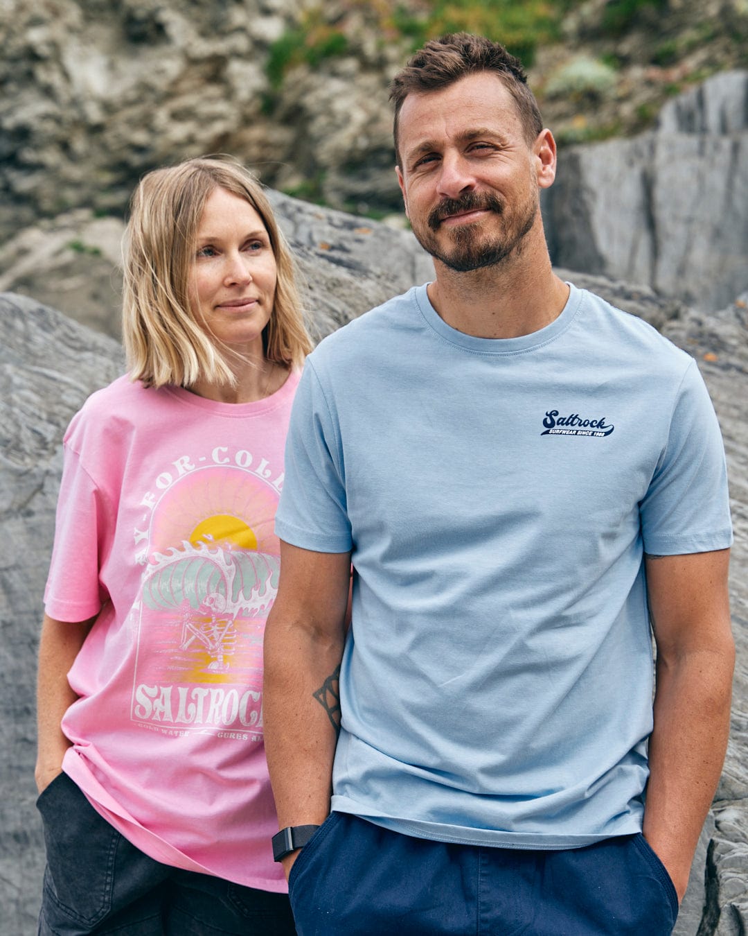 Two people wearing casual Saltrock Home Run - Mens T-Shirts - Blue, one in light blue, stand outdoors against a rocky backdrop in 100% cotton comfort.