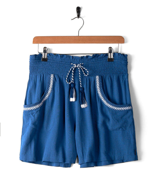 A pair of Jonie - Womens Shorts - Blue from Saltrock, hanging on a wooden hanger against a white background.