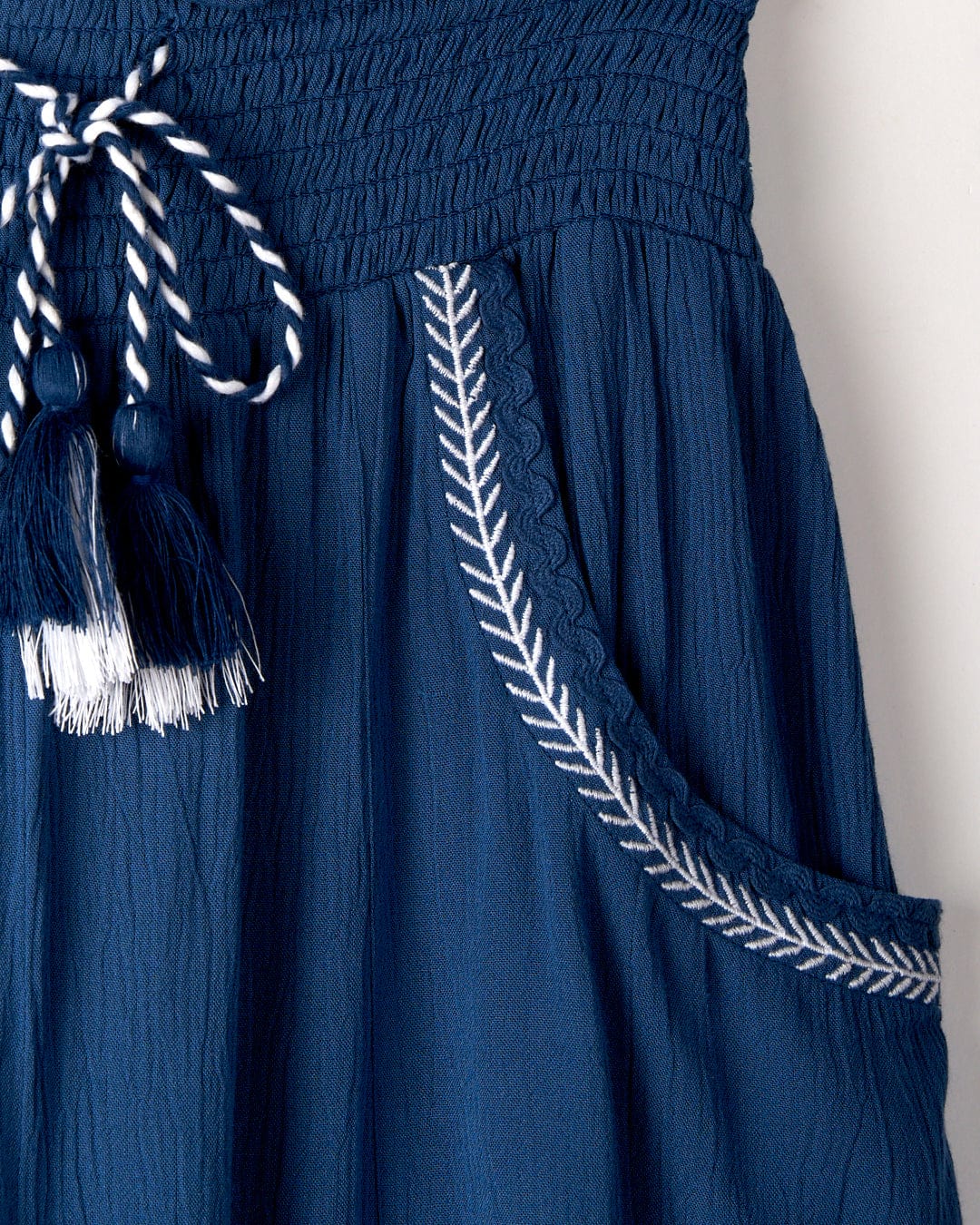 Close-up of the top of the Jonie - Womens Trouser - Blue from Saltrock, made from lightweight crinkle viscose, featuring a high waist drawstring with tassels and a simple white decorative zigzag trim along the pocket.