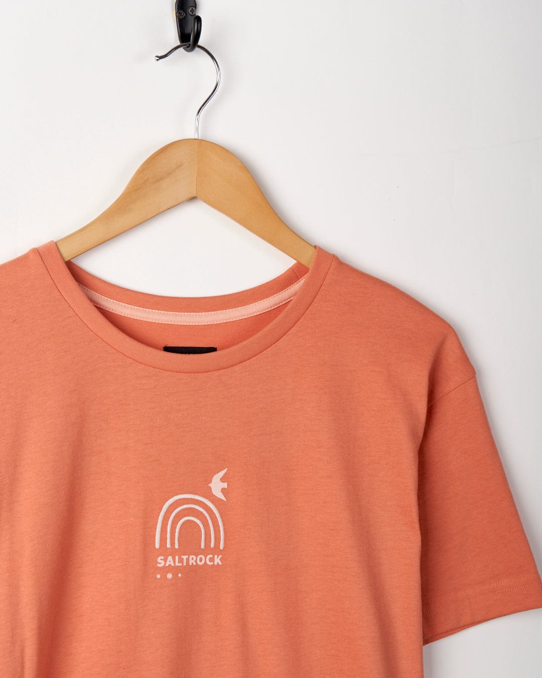 Journey - Recycled Womens Short Sleeve T-Shirt in Peach with a "Saltrock" logo embroidered on recycled polyester, hanging on a wooden hanger against a white background.