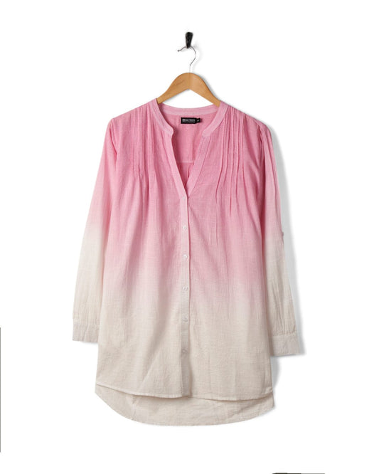 A long-sleeve, button-down shirt with a pink dip dye gradient, hanging on a wooden hanger against a white background. The Saltrock Karthi - Womens Long Sleeve Shirt - Pink/White boasts an oversized fit and is made from lightweight cotton material for ultimate comfort.
