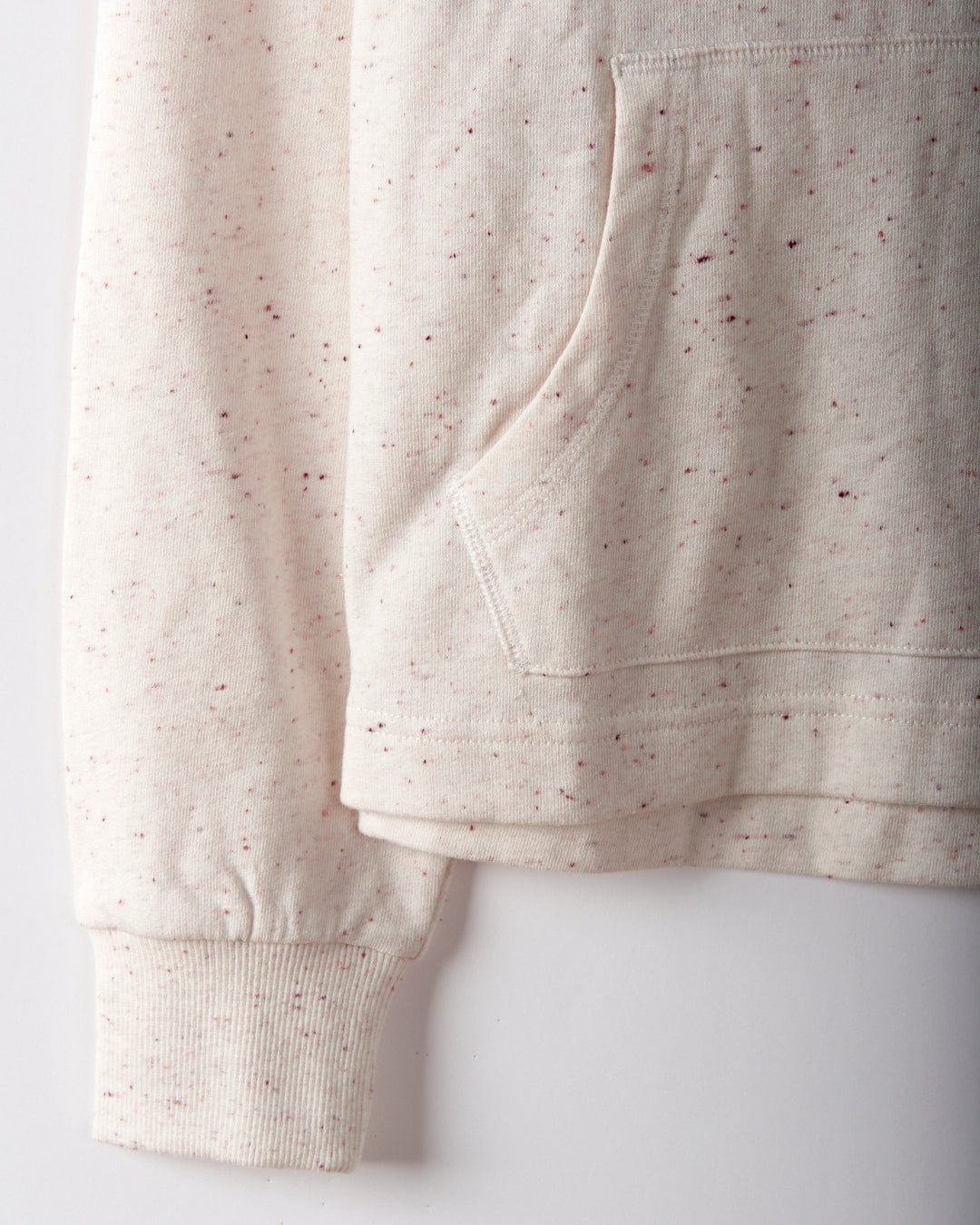 Close-up of the Kellie Women's Cropped Pop Hoodie in cream, featuring a light beige speckled design, ribbed cuffs, a kangaroo pocket, and Saltrock's signature puffed print against a plain background.