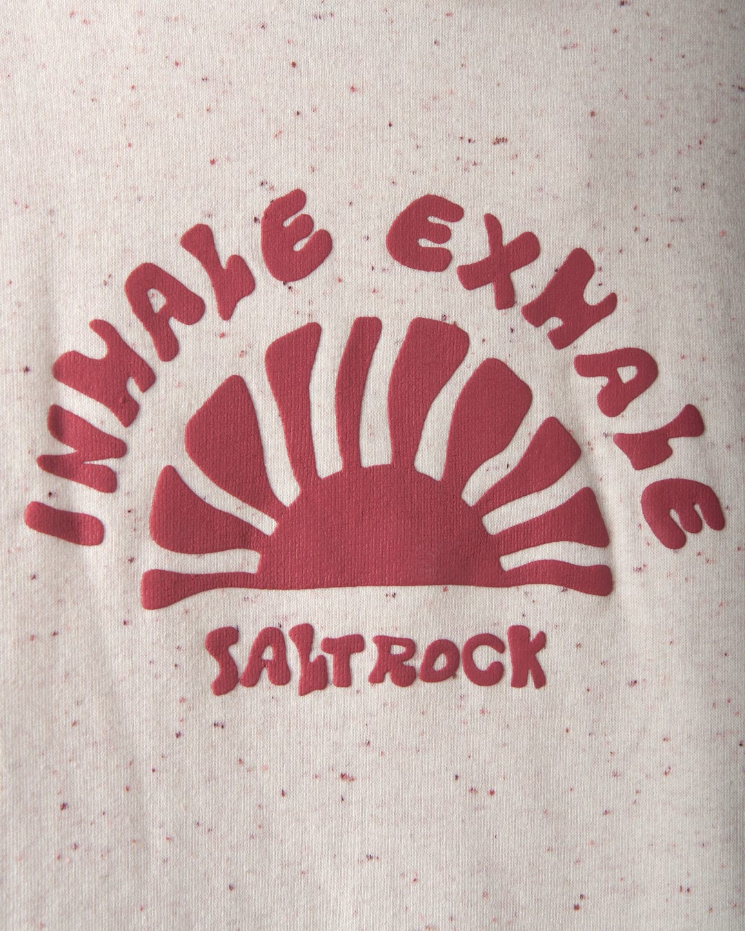 Red graphic with a stylized sun and the phrase "INHALE EXHALE SALTROCK" in the Saltrock puffed print on a speckled, cream-colored background of the Kellie - Women's Cropped Pop Hoodie by Saltrock.