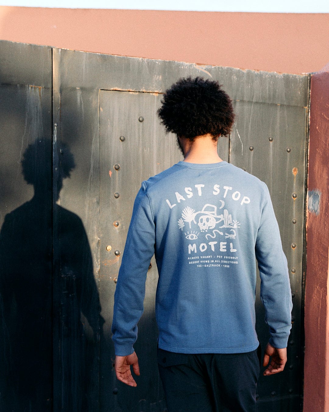 A person with an afro standing with their back to the camera, wearing a Saltrock blue sweatshirt with 