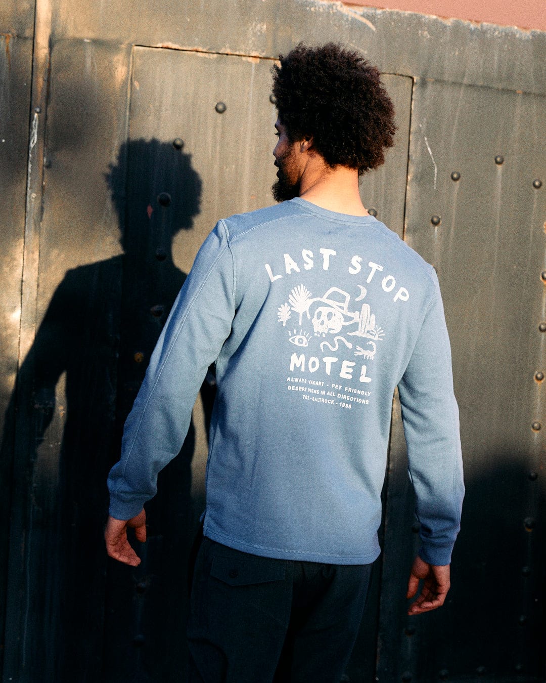 A man with an afro facing away from the camera, wearing a blue Saltrock sweatshirt made of peached soft material with 