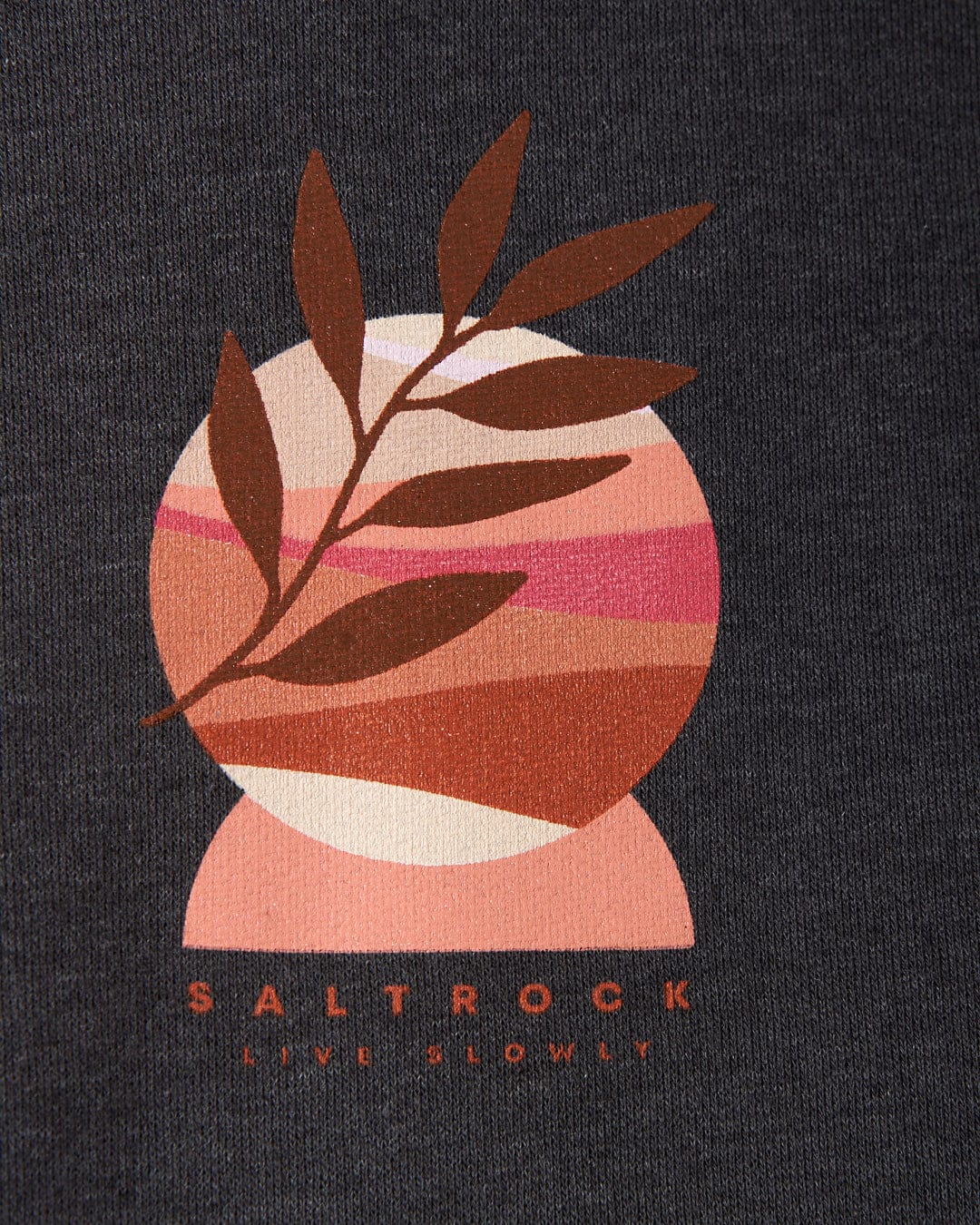 A minimalist graphic design featuring a pink and orange circular shape with a brown branch overlay, embodying the distinct Saltrock branding. The text below reads "SALTROCK LIVE SLOWLY" on a dark background, reminiscent of serene sunset graphics. This design is showcased on the Live Slowly Women's Pop Hoodie in Grey by Saltrock.