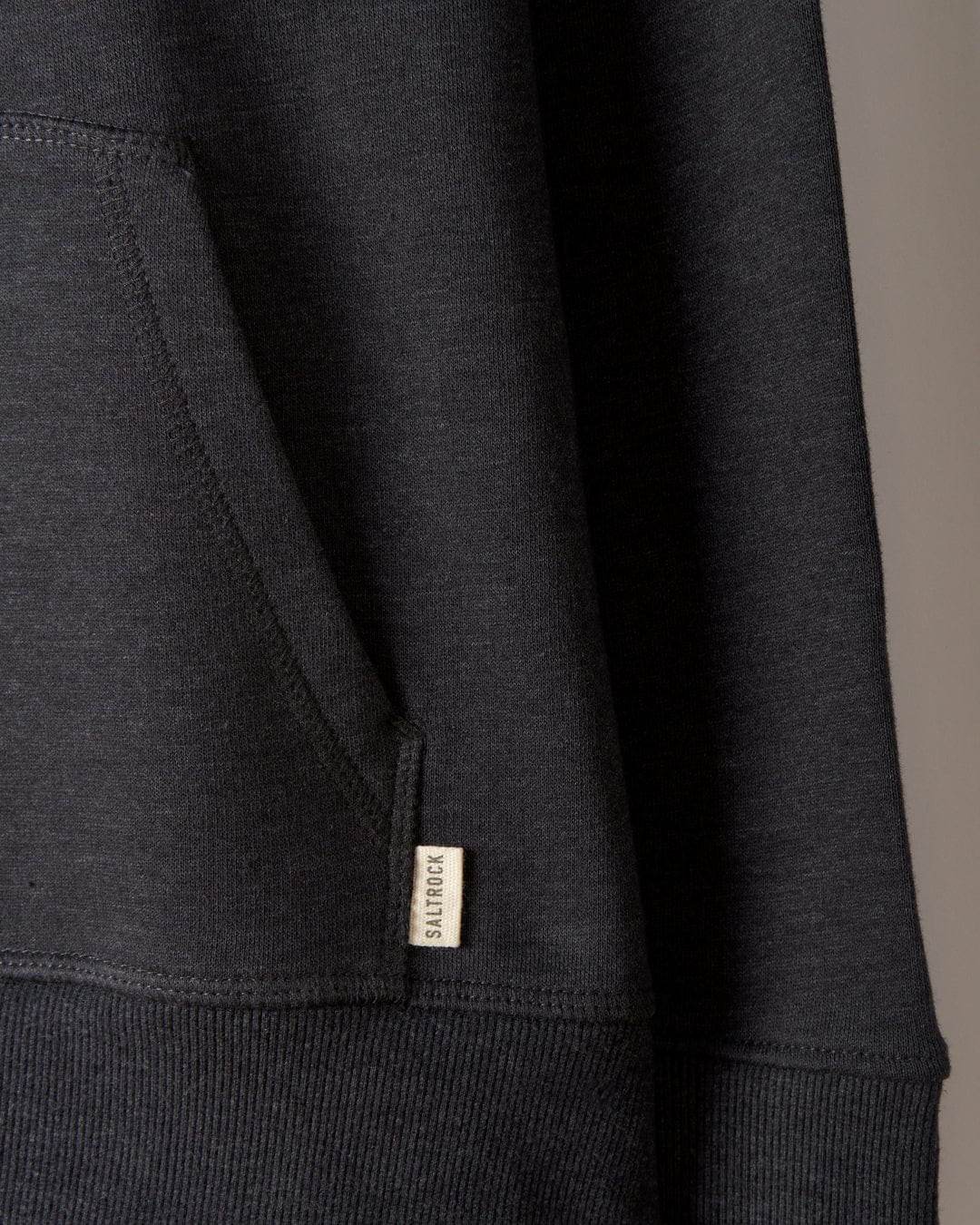 Close-up of the Live Slowly - Women's Pop Hoodie in grey, showcasing a visible front pocket with a small tag labeled "SOLIDITY" attached near the pocket seam. The design features subtle Saltrock branding, adding an extra touch of style.