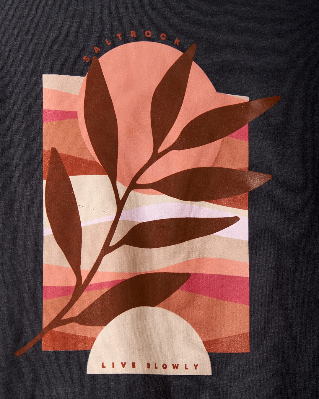 The "Live Slowly - Womens Pop Hoodie - Grey" by Saltrock features a graphic design on dark fabric, showcasing a stylized brown leaf with the brand name "Saltrock" at the top and the slogan "Live Slowly" at the bottom. The background incorporates wavy, earthy color segments that evoke sunset graphics, enhancing Saltrock's distinctive branding.