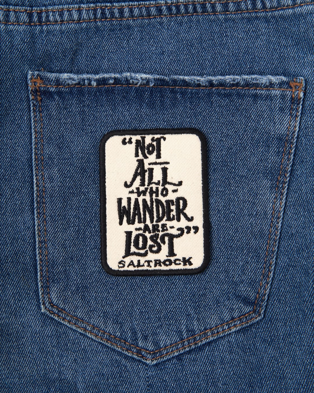 An Lost Ships iron on patch in a jeans pocket that says not all wander lost.