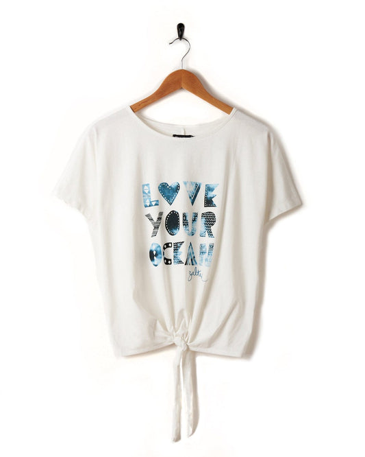 A Saltrock Love Your Ocean - Recycled Womens T-Shirt - White with "LOVE YOUR OCEAN" printed on the front in blue, crafted from recycled material. It features a tied knot at the bottom and a loose fit, hanging on a wooden hanger against a white background.