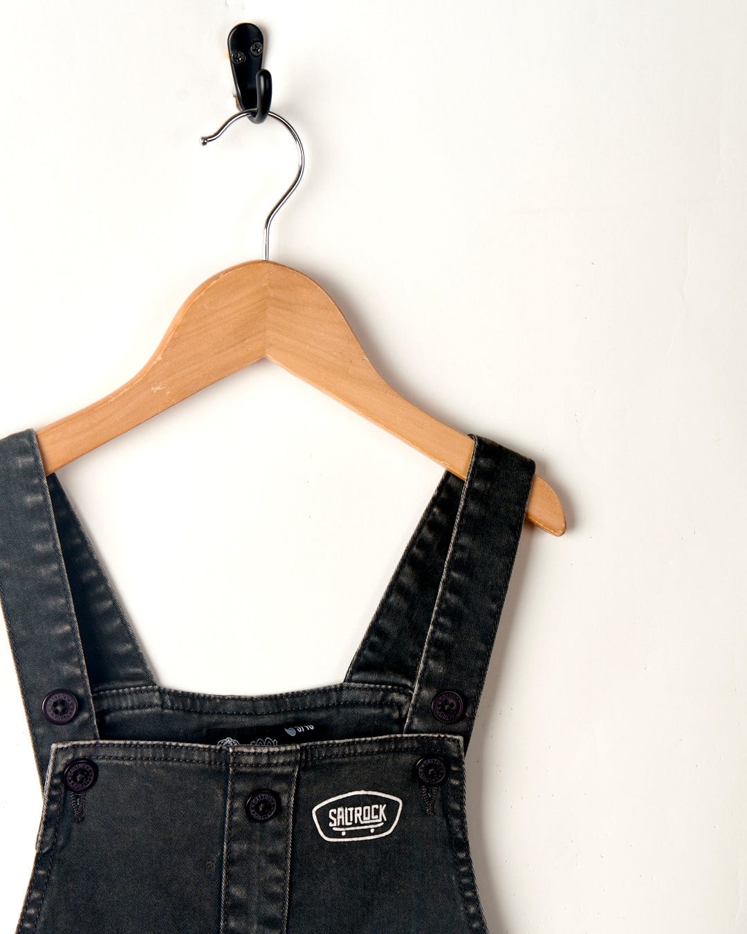 Saltrock Lyn-Z - Kids Dungarees - Washed Black with adjustable straps hanging on a wooden hanger against a plain white background.