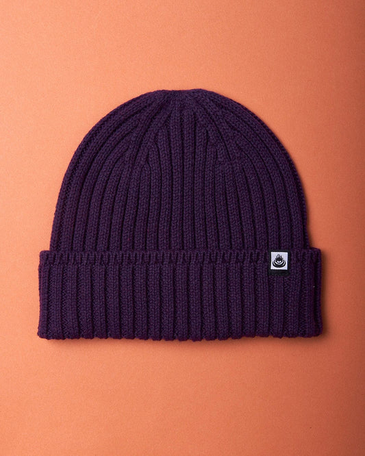 A Saltrock Maine - Fisherman Beanie - Dark Purple on an orange background.